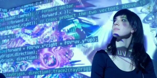 A woman in long dark hair stands against a wall against which computer codes and abstract purple and blue images are projected