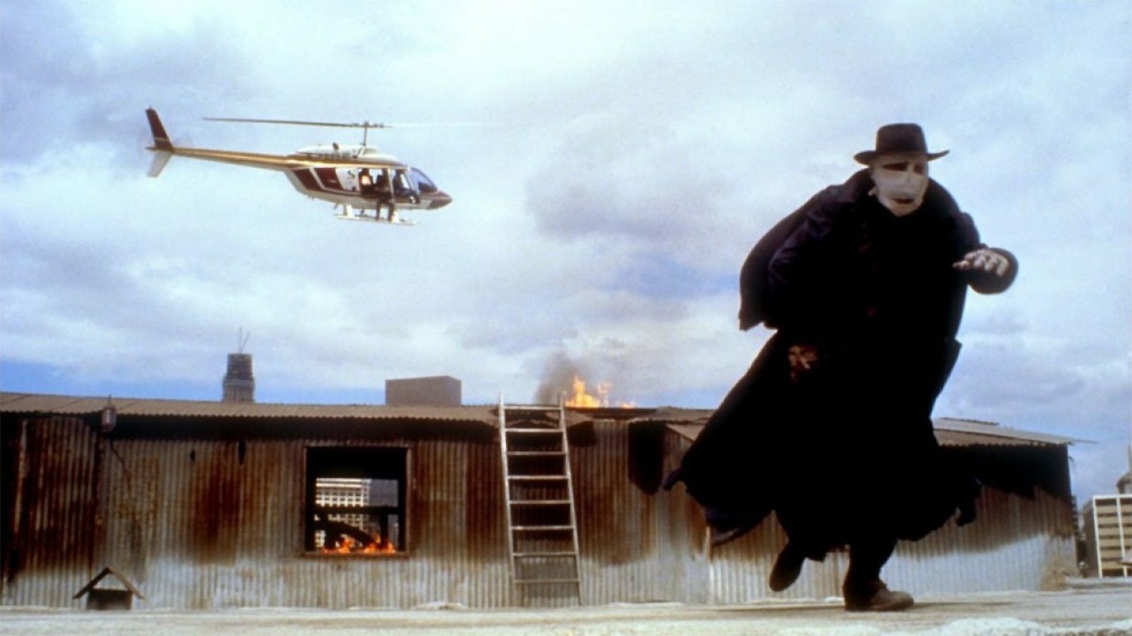 A masked and cloaked man runs from a helicopter