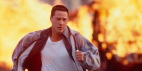 A man wearing a t-shirt and jacket and khakis runs from a blazing explosion in the background