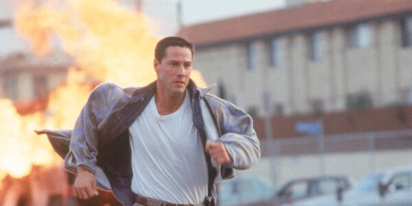A man wearing a t-shirt and jacket and khakis runs from a blazing explosion in the background