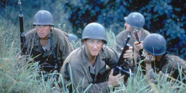 Four soldiers in fatigues and helmet crouch in a field of tall grass