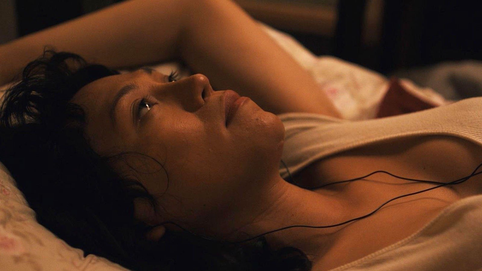 A woman lying down in bed with her arm extended above her head and wearing a meditative expression