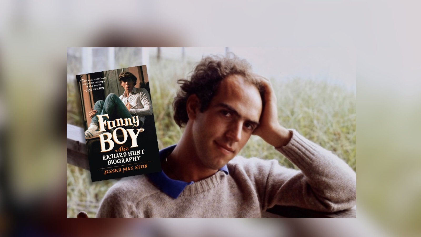 A man with curly hair, a beige sweater and blue shirt underneath poking through the collar, sits with his hand propping up his head, smiling mildly. Next to him is a floating image of a book titled FUNNY BOY: THE RICHARD HUNT BIOGRAPHY